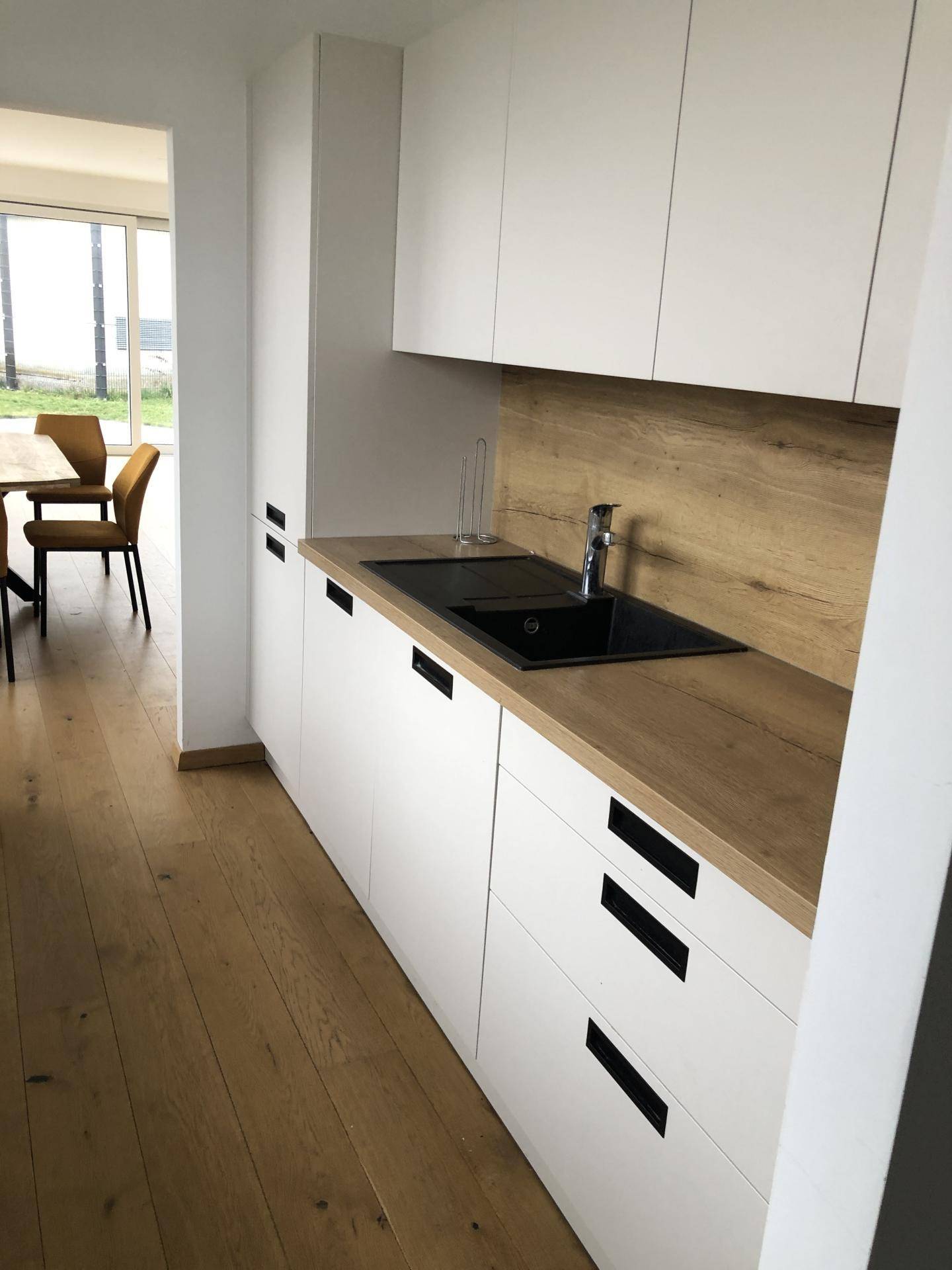 Moderne Küche mit schwarzer Spüle, Holzarbeitsplatte und Zugang zum Essbereich.