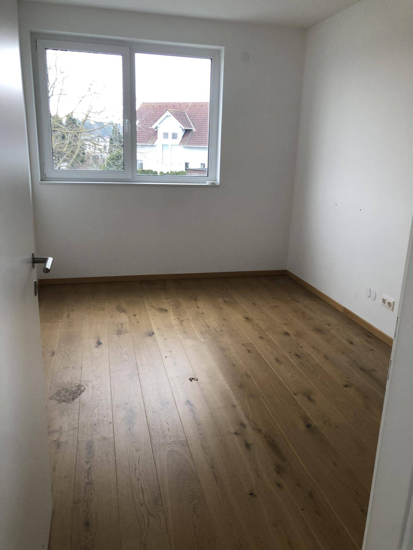 Helles Zimmer mit Holzboden und Blick aus dem Fenster auf die Umgebung.