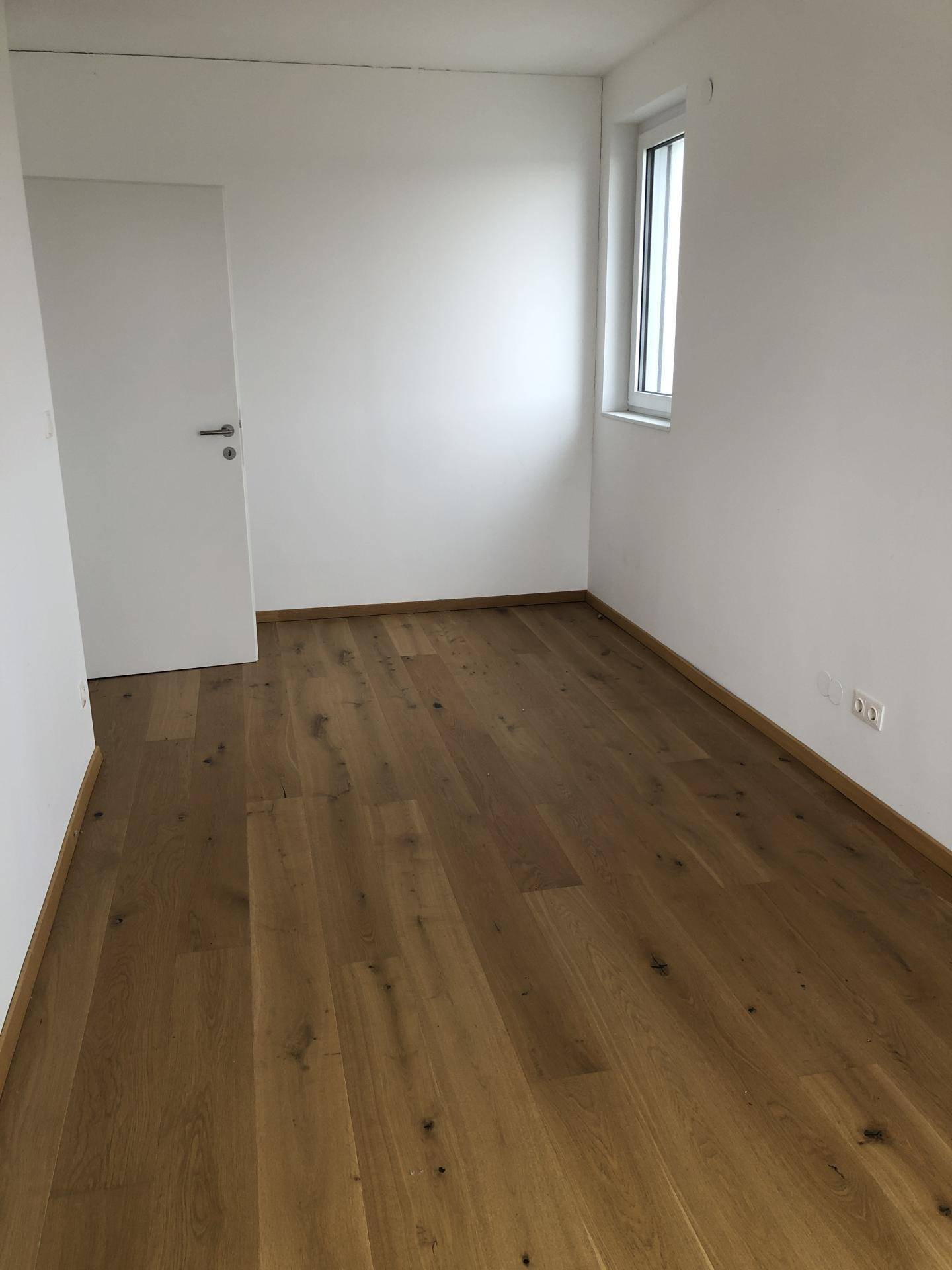 Leeres Zimmer mit Holzboden und Fenster, ideal als Schlaf- oder Arbeitszimmer.