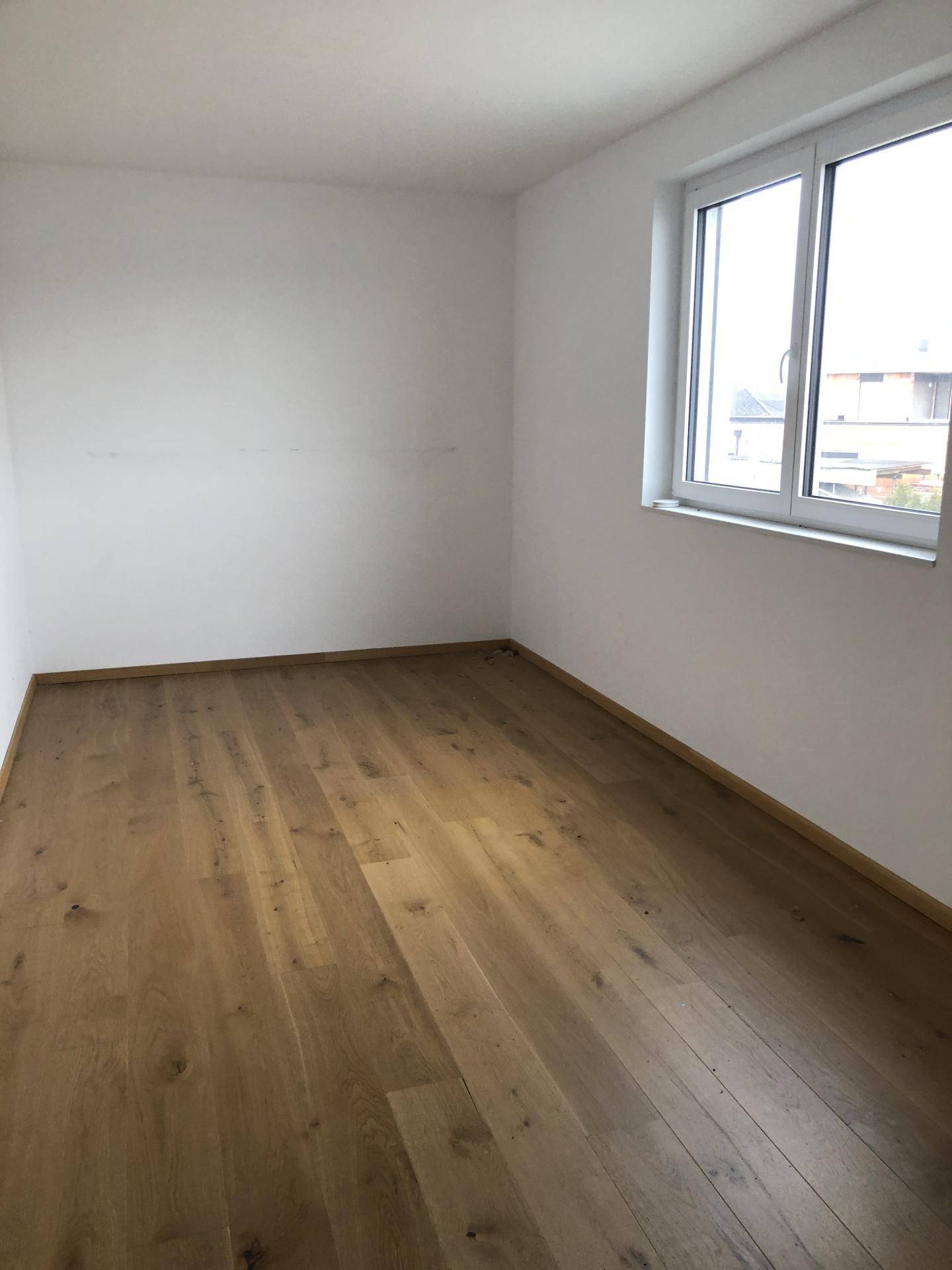 Helles Zimmer mit Holzboden und großem Fenster, das viel Tageslicht hereinlässt.