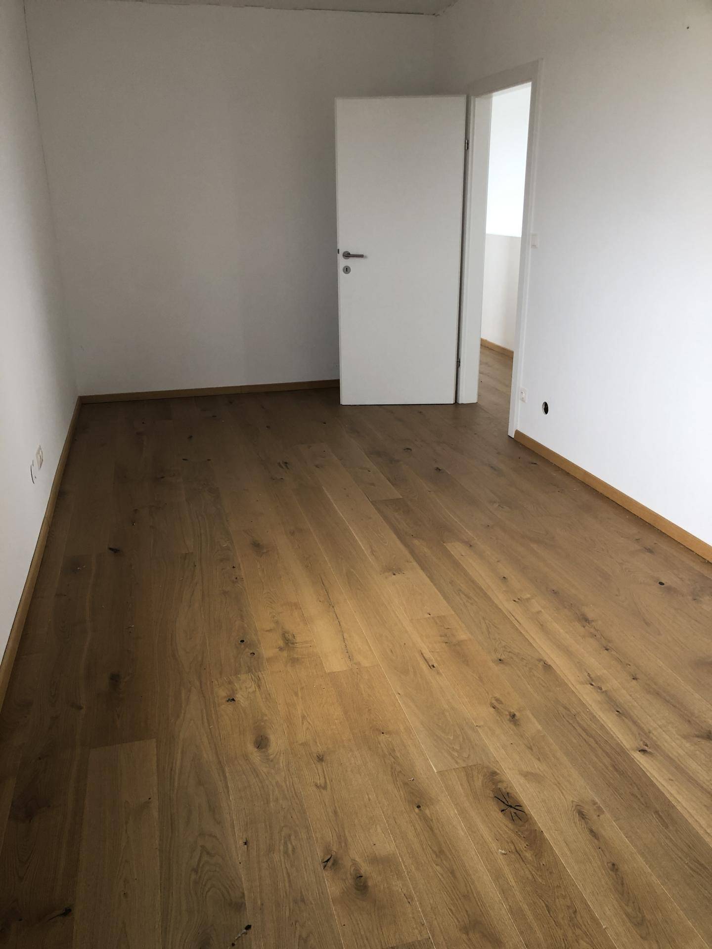 Leeres Schlafzimmer mit hellem Holzboden und weißen Wänden, bereit zur Einrichtung.