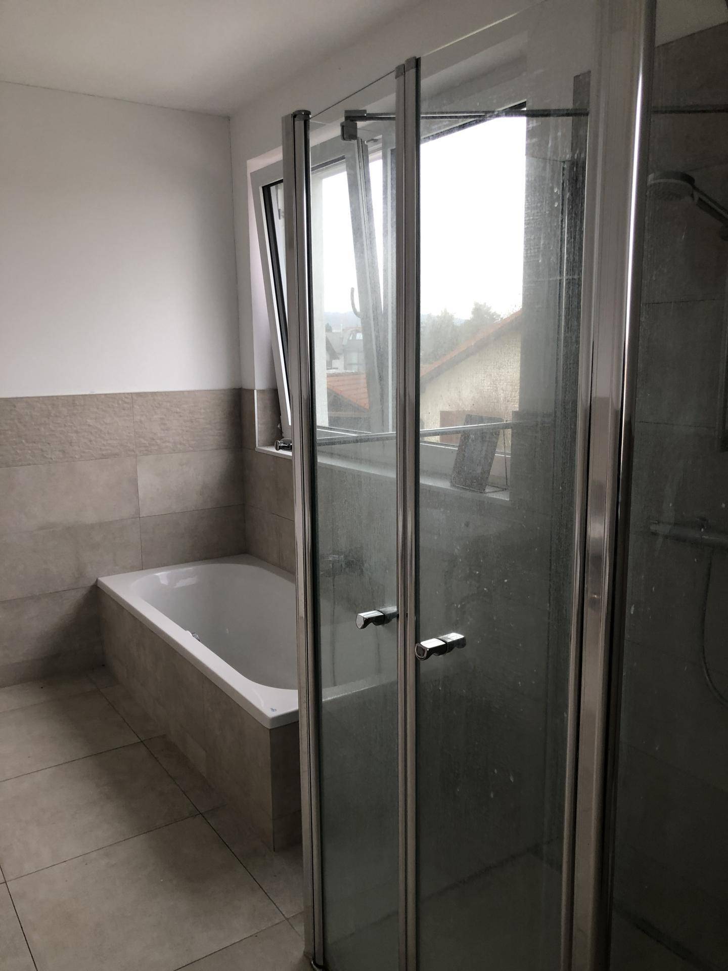 Modernes Badezimmer mit Badewanne, Duschkabine und Fenster für Tageslicht.