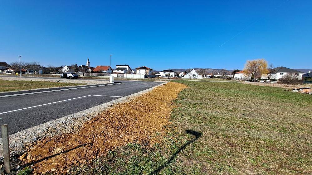 Großes Grundstück neben einer asphaltierten Straße mit Blick auf umliegende Häuser und einen Kirchturm.