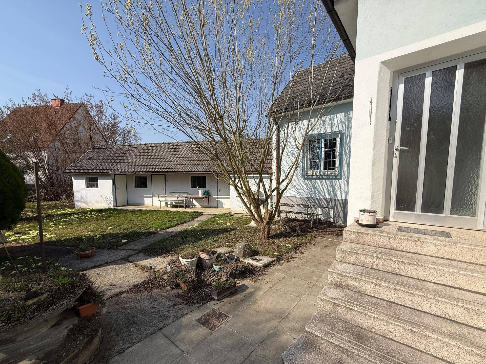 Eingangsbereich des Hauses mit Treppe und Blick auf den Garten mit Nebengebäude.
