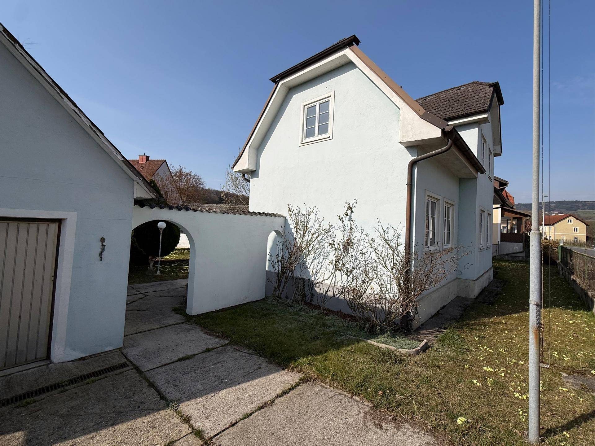Seitenansicht des hellblauen Hauses mit Garage und gepflasterter Zufahrt.
