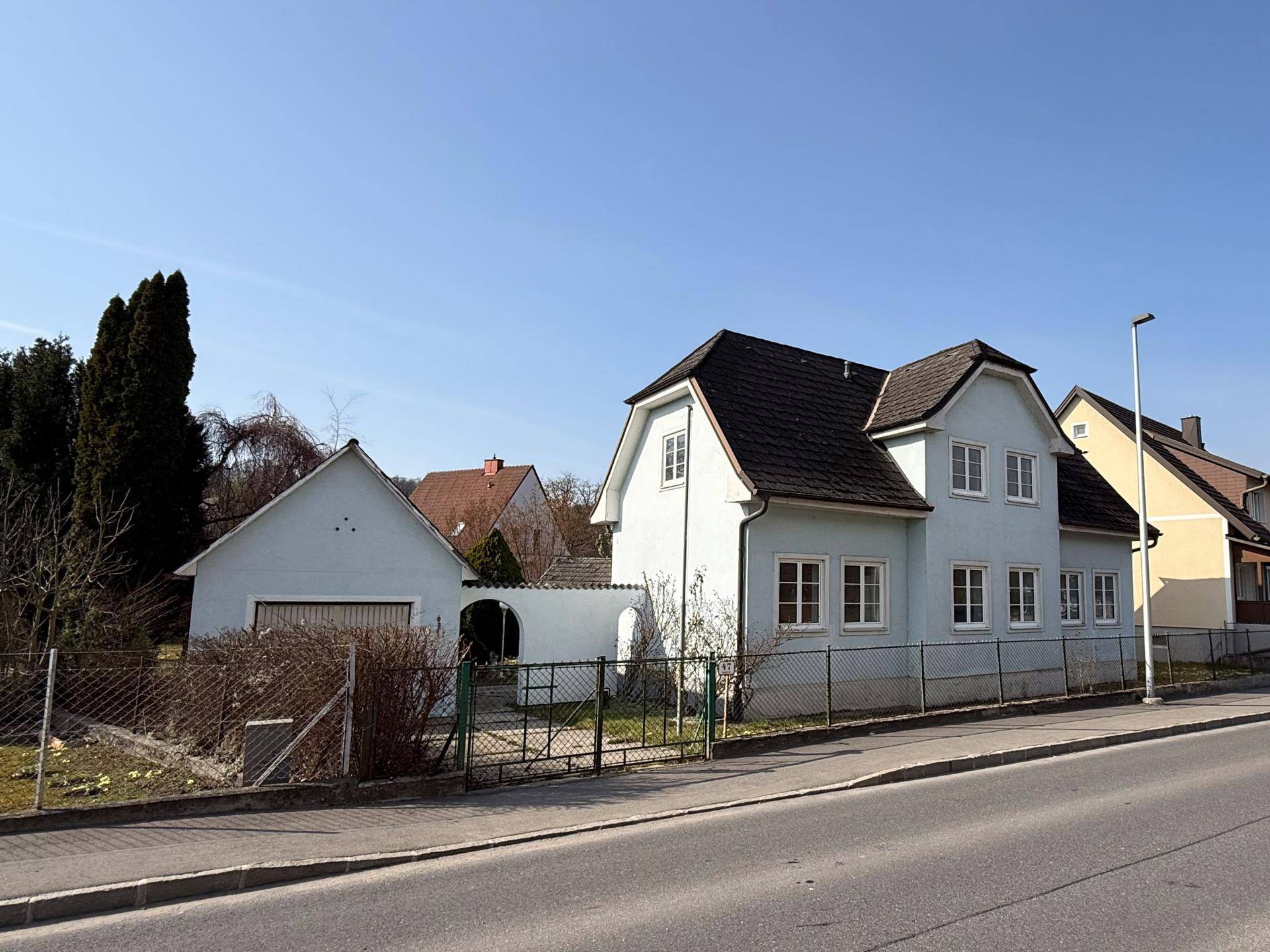 Ansicht des Hauses von der Straße mit Zaun, Garage und gepflegtem Vorgarten.