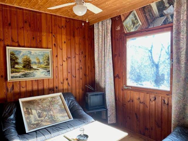 Gemütliches Wohnzimmer mit Holzvertäfelung, Deckenventilator und einfacher Einrichtung im Vintage-Stil.