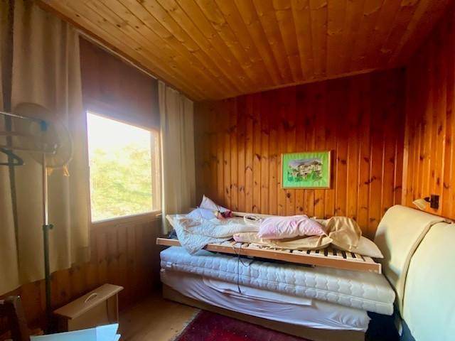 Schlafzimmer mit Holzvertäfelung, einem Bett und einem Fenster, das viel natürliches Licht hereinlässt.