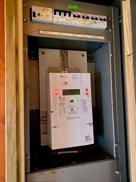 Elektrischer Sicherungskasten mit Zähler und verschiedenen Schaltern in einem Holzrahmen an der Wand.