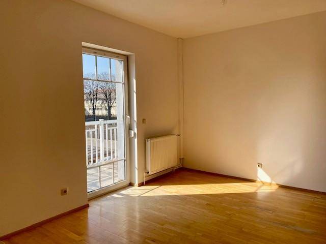 Sonniger Raum mit Parkettboden und Balkontür, bietet viel Tageslicht und einen angenehmen Ausblick.