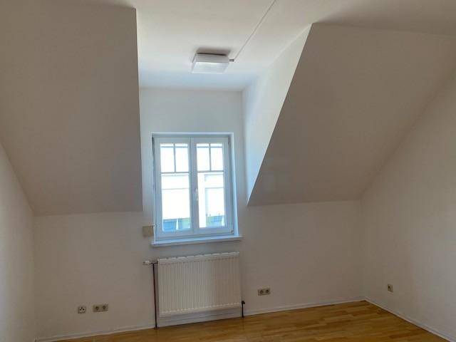 Gemütliches Zimmer im Dachgeschoss mit schrägen Wänden, Fenster und Parkettboden, hell und ruhig gelegen.