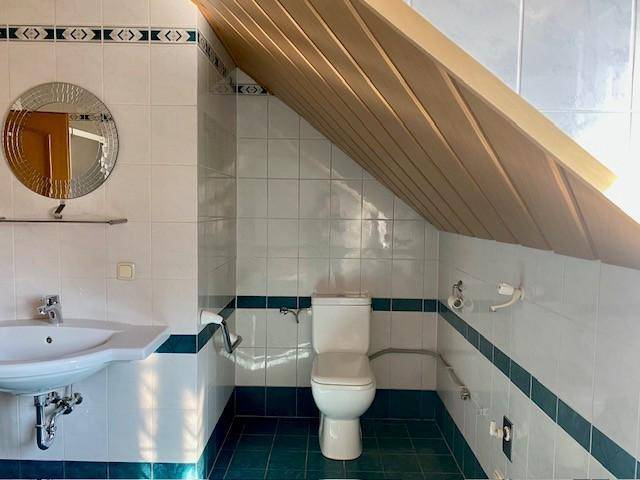 Separater WC-Bereich im Badezimmer mit Waschbecken, Toilette und schräger Holzdecke, hell gefliest.