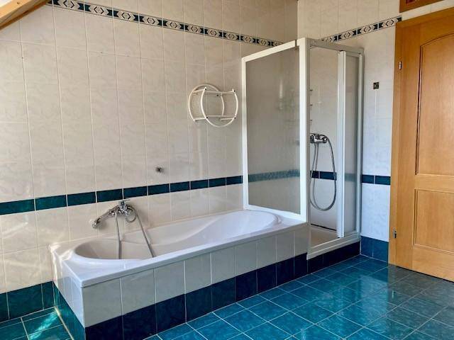 Badezimmer mit Badewanne und Duschkabine, blauen Bodenfliesen und weißer Wandverkleidung, funktional ausgestattet.