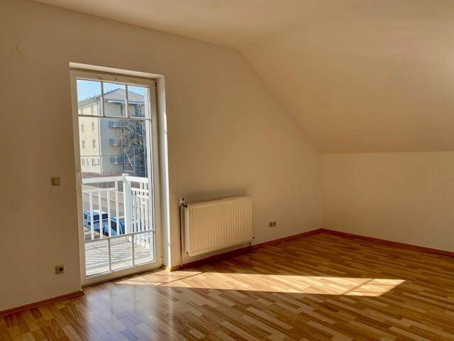 Helles Zimmer mit Parkettboden und Zugang zu einem Balkon, ideal als Schlaf- oder Wohnraum, sonnendurchflutet.