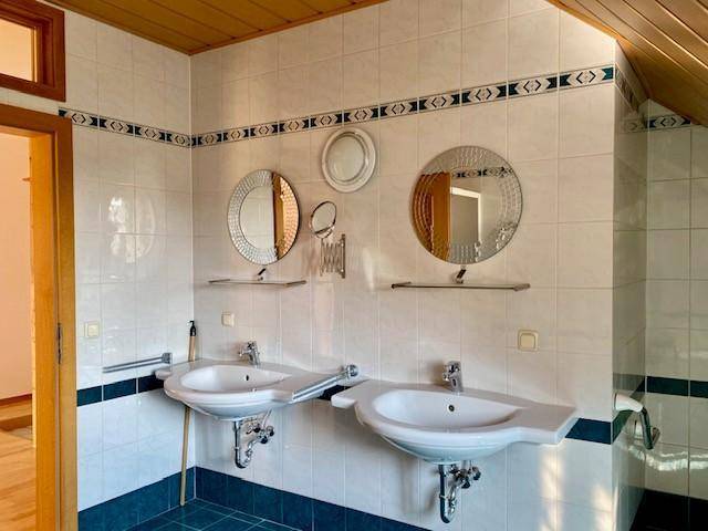 Badezimmer mit Doppelwaschbecken, runden Spiegeln und blauen Akzentfliesen unter einer Holzdecke.