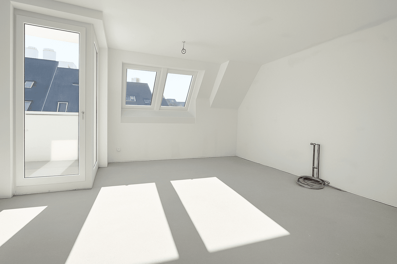 Heller, leerer Raum mit weiß gestrichenen Wänden, Dachschrägen und Zugang zu einem Balkon.
