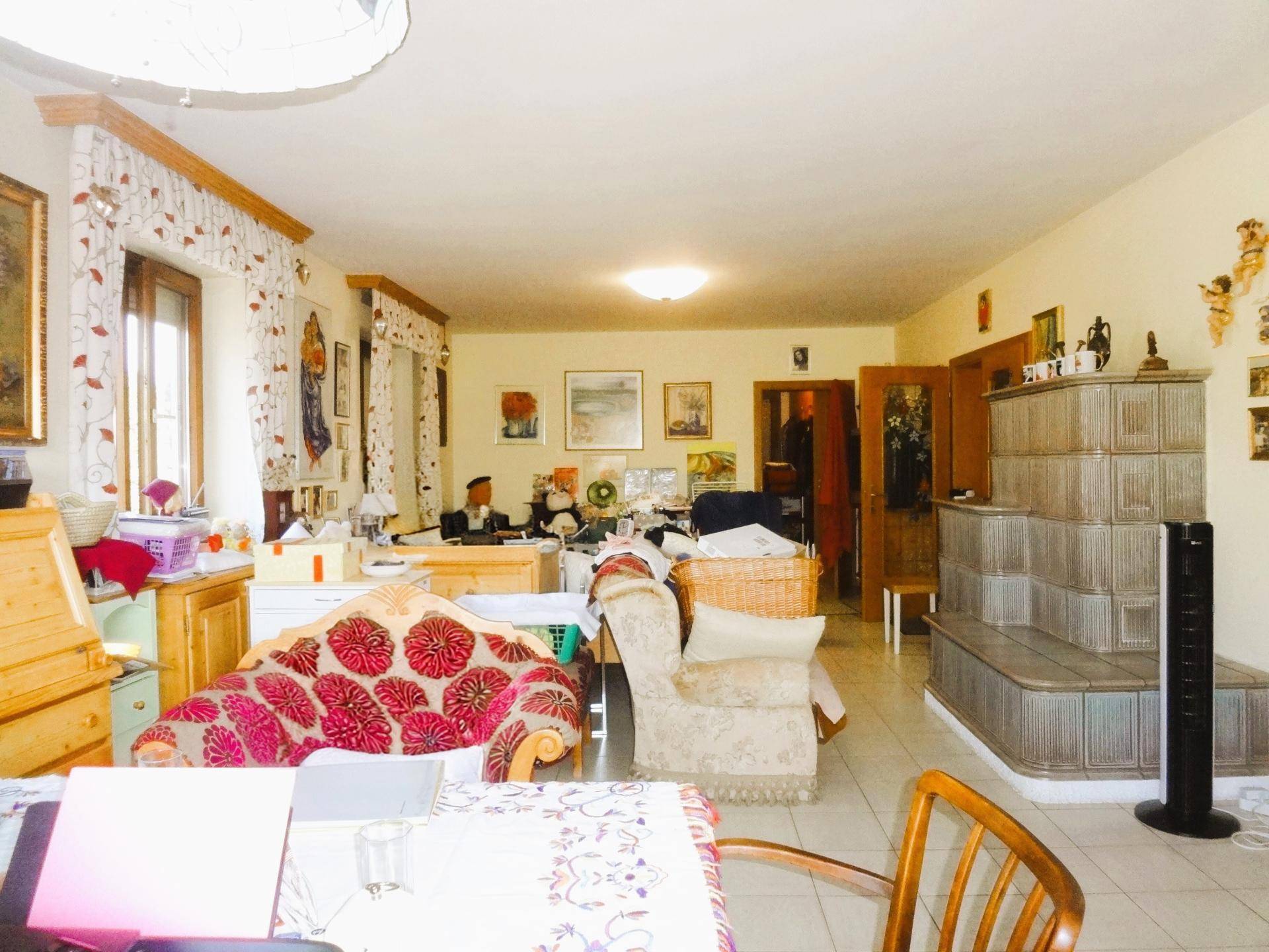 Geräumiges Wohnzimmer mit Kachelofen, Fliesenboden und vielen persönlichen Gegenständen.