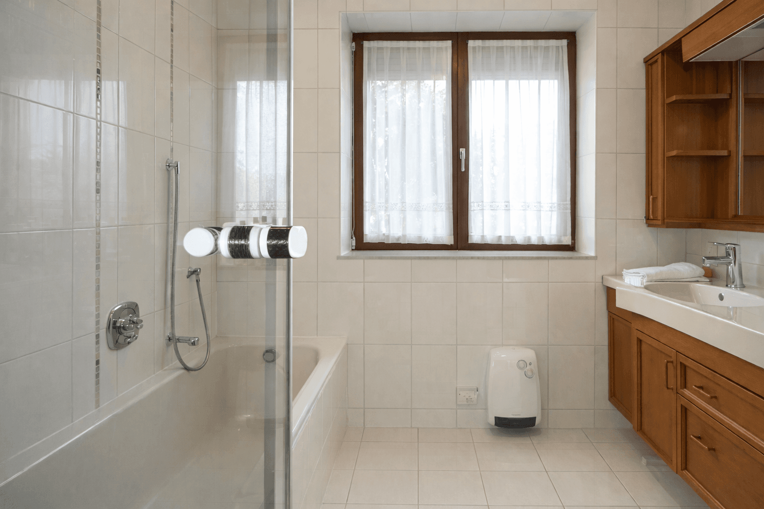 Helles Badezimmer mit Badewanne, Duschabtrennung, Fenster und Holzwaschtisch.