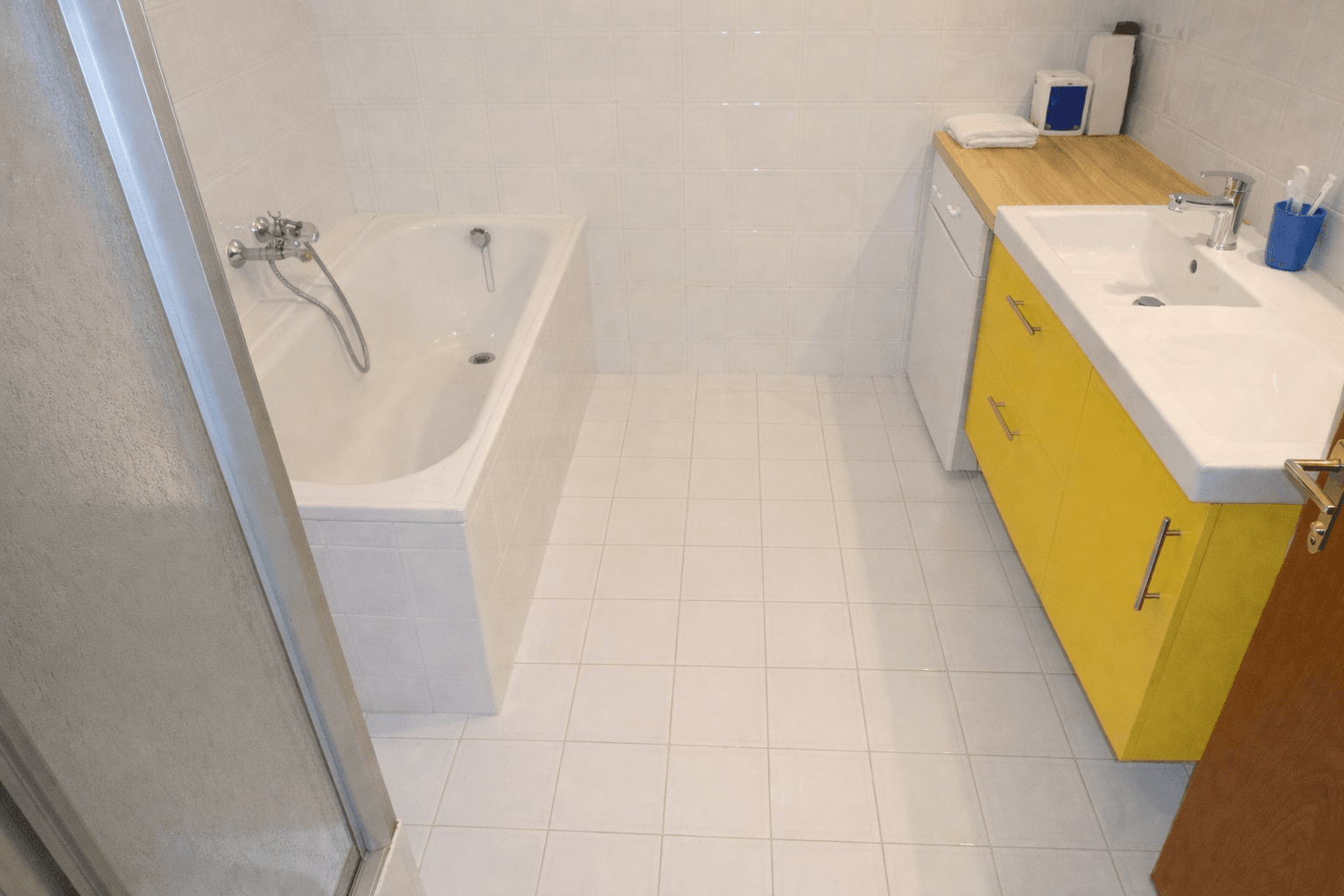 Modernisiertes Badezimmer mit Badewanne, gelbem Waschtischunterschrank und Fliesenboden.