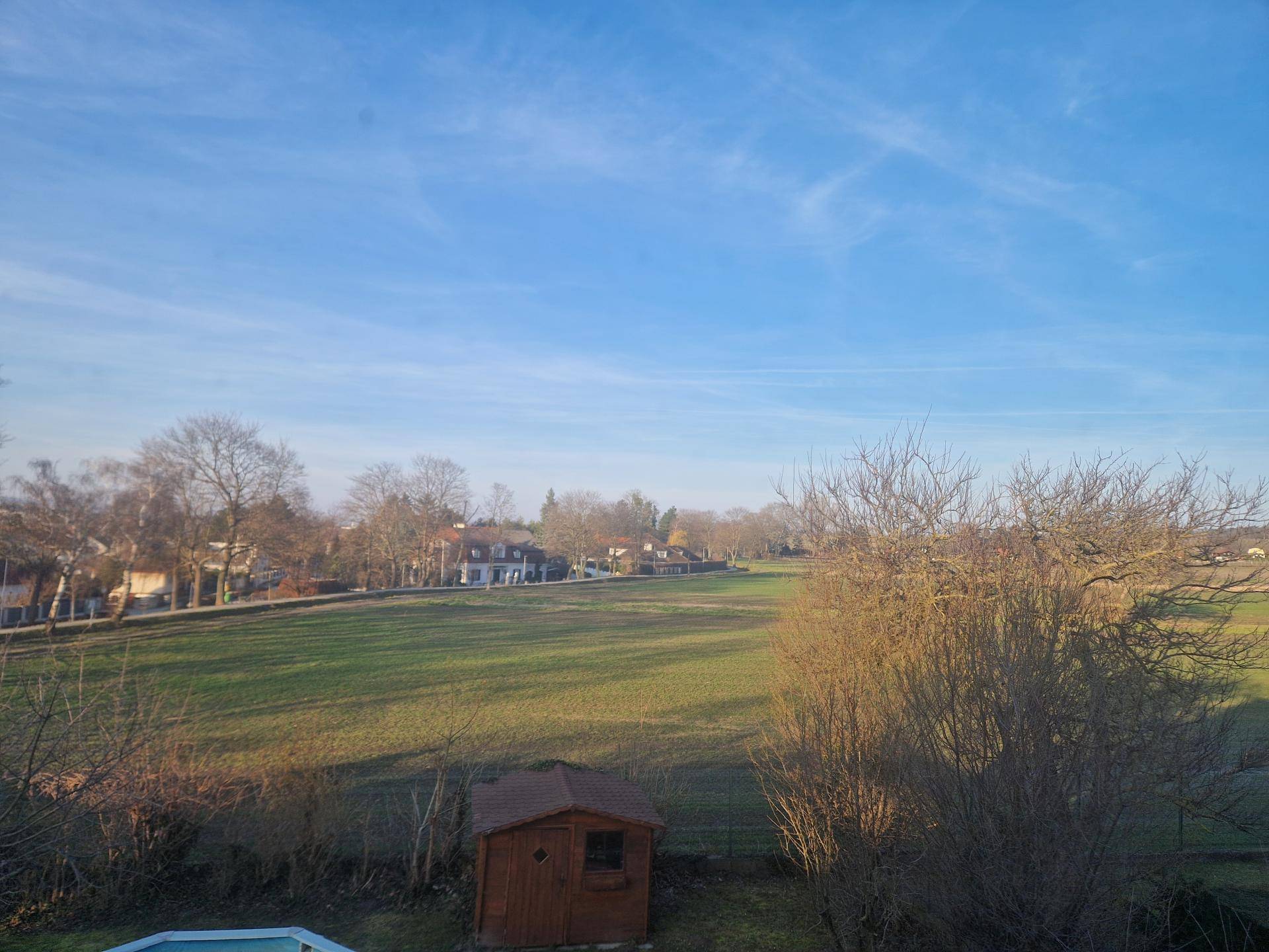 Weitläufiger Blick über grüne Felder und Bäume unter einem klaren blauen Himmel.