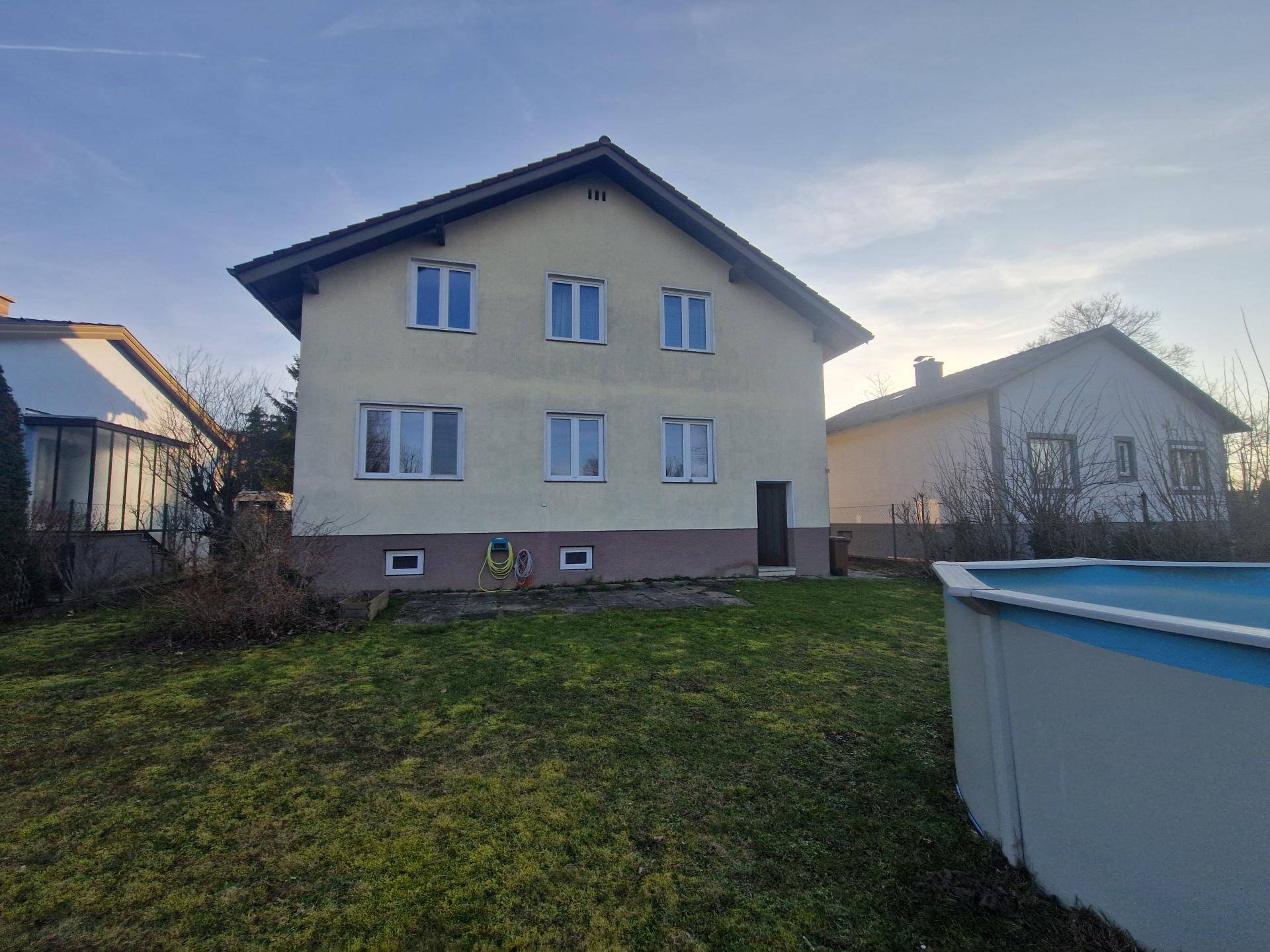 Rückseite des gelben Hauses mit Garten, Aufstellpool und Rasenfläche im Sonnenlicht.