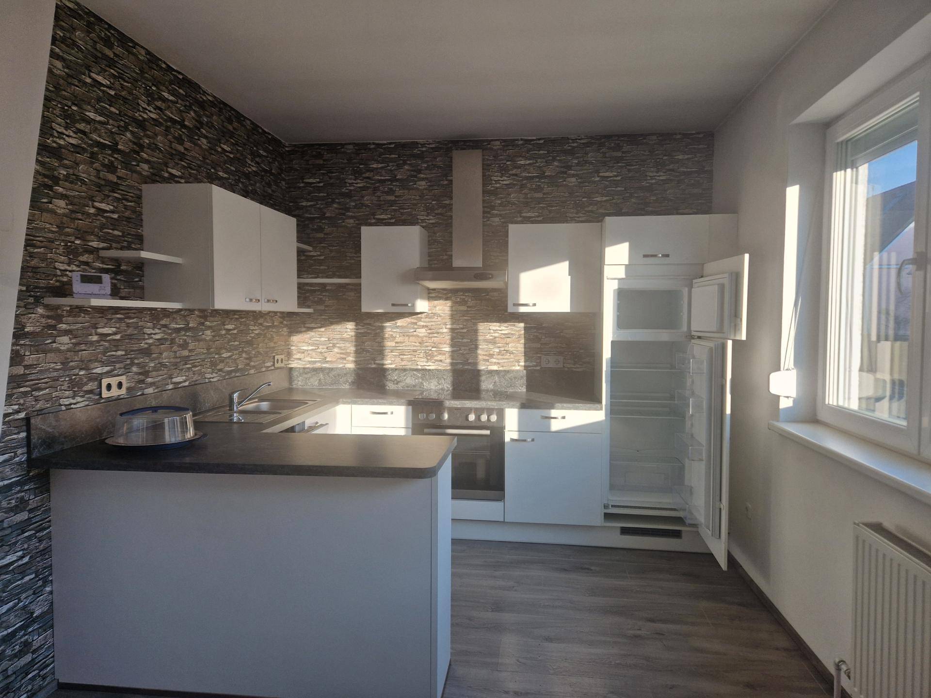 Moderne Küche mit weißen Schränken, Steinwand und Laminatboden, hell beleuchtet.