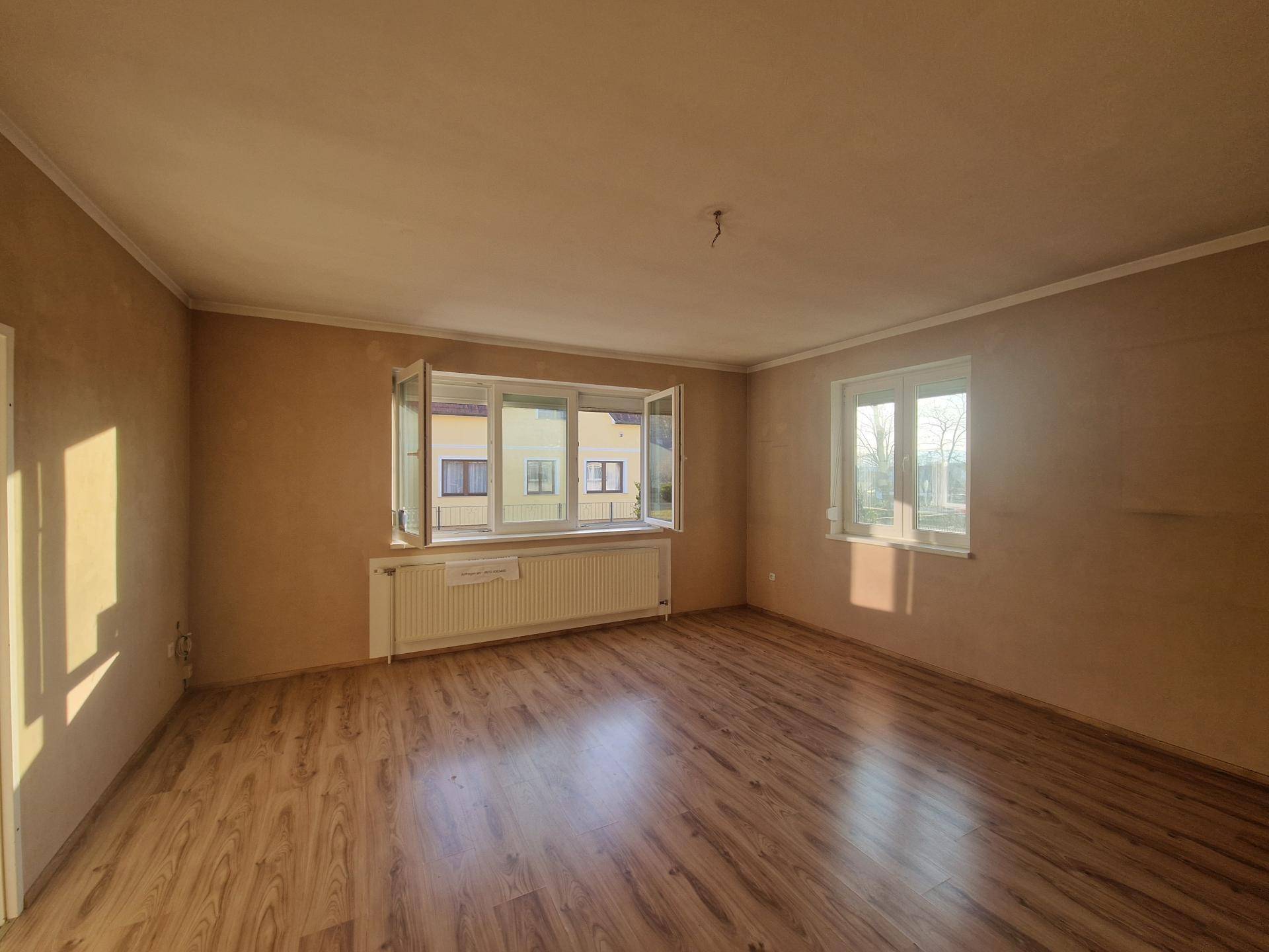 Helles Wohnzimmer mit Laminatboden und großen Fenstern, sonnendurchflutet und geräumig.