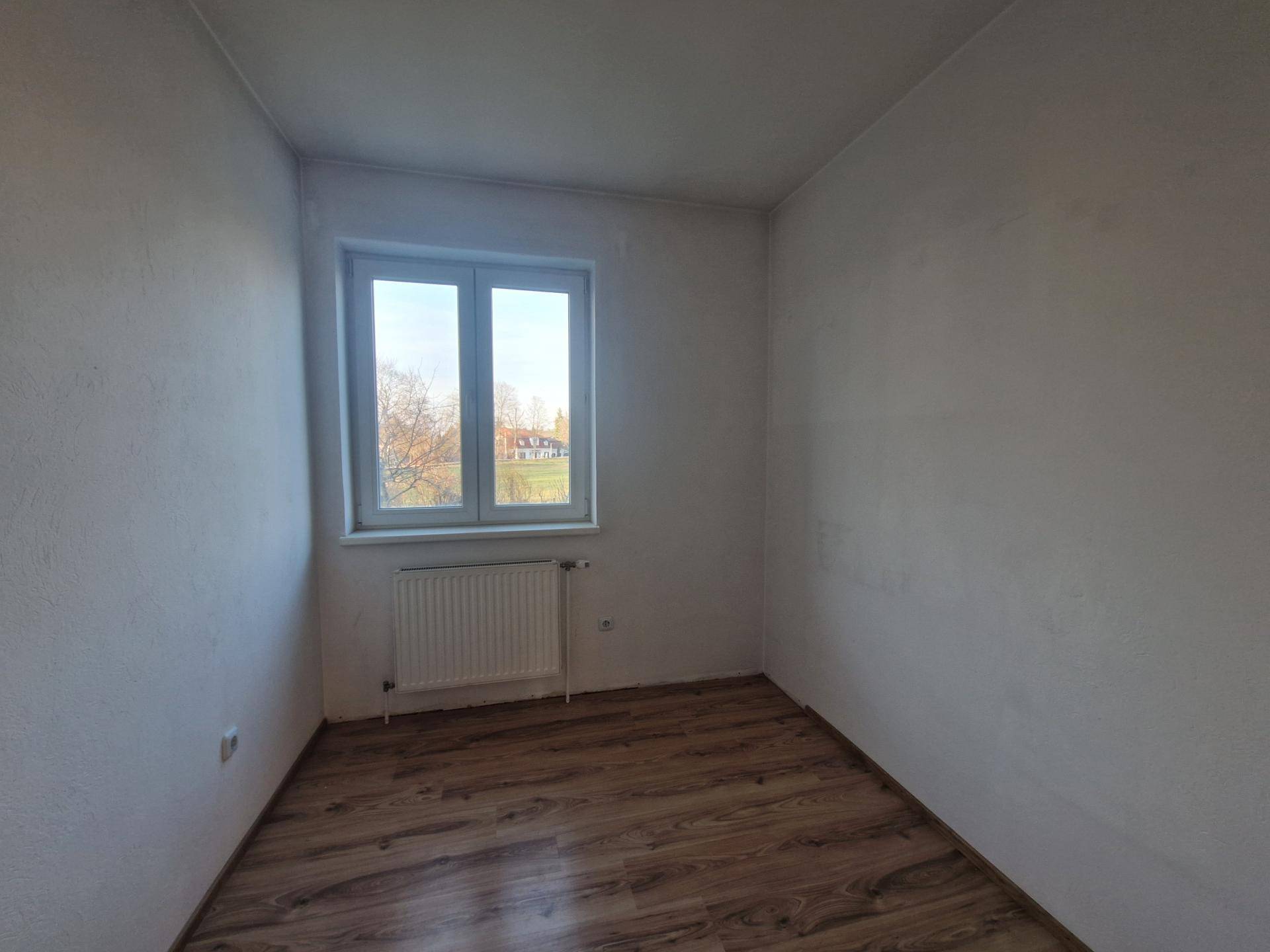 Helles Zimmer mit Laminatboden und einem Fenster, ideal als Schlaf- oder Arbeitszimmer.