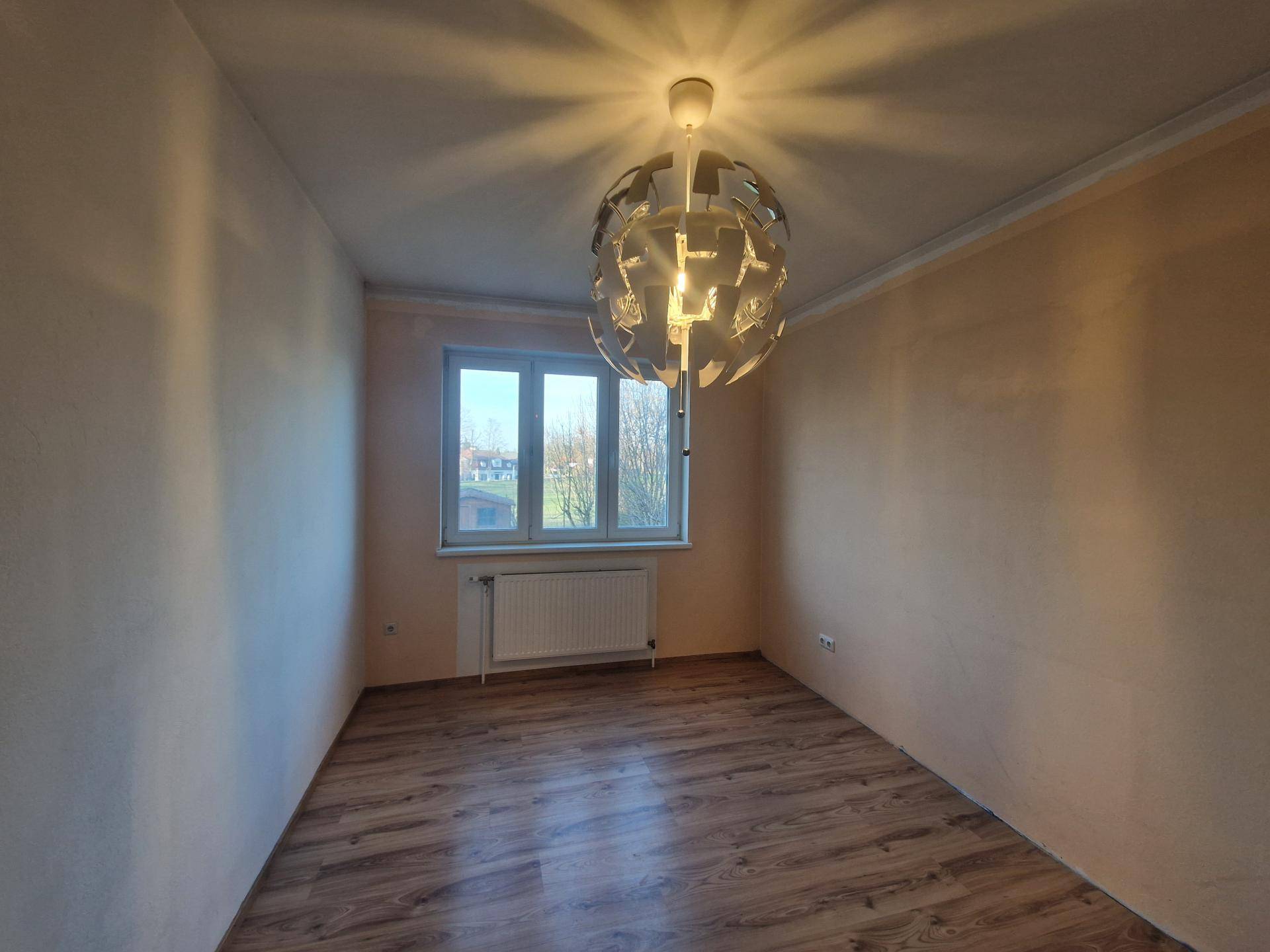 Helles Zimmer mit Laminatboden, Fenster und moderner Deckenleuchte, gut gepflegt.