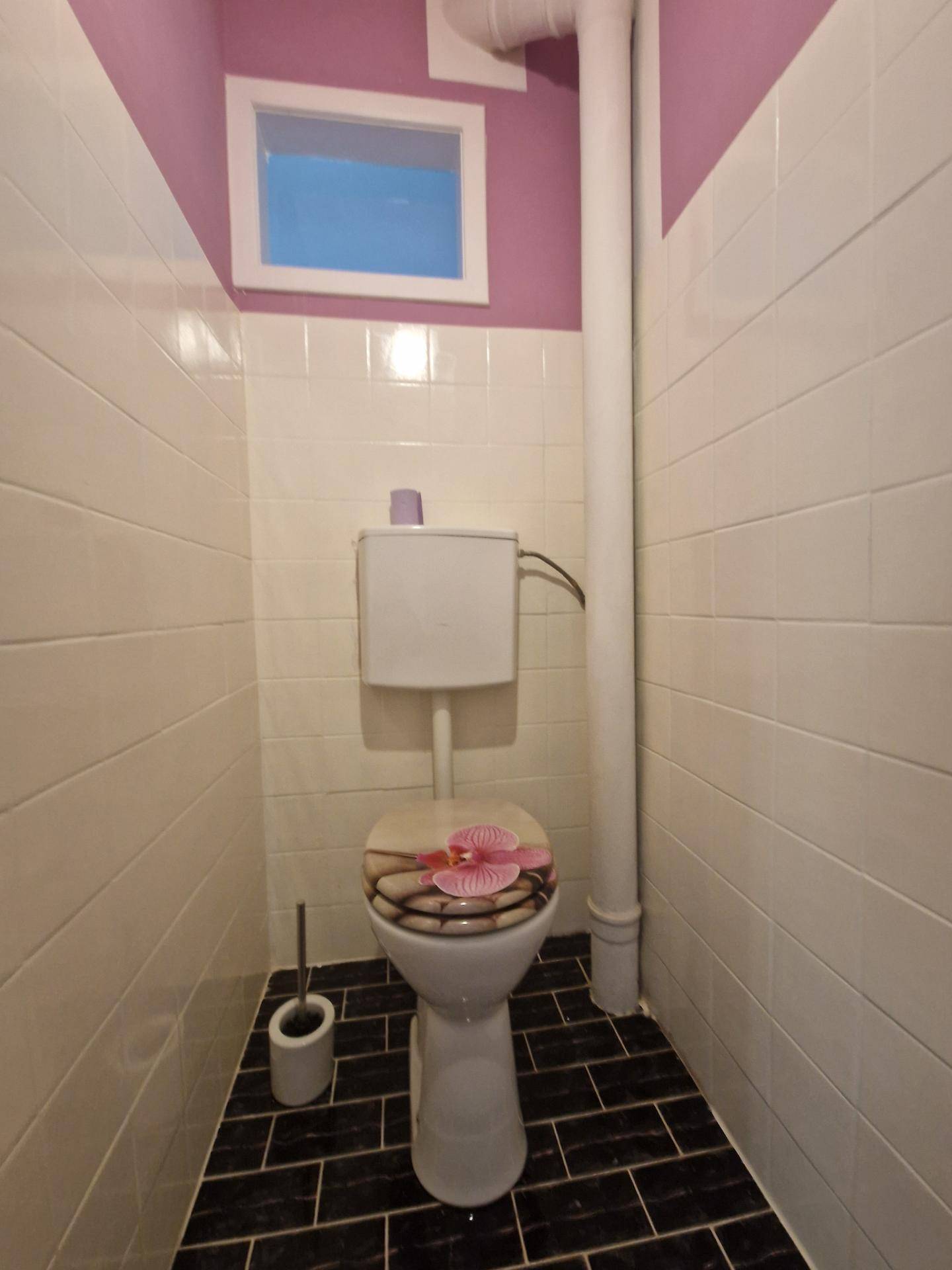 Separate Toilette mit dunklem Fliesenboden und kleinem Fenster, sauber und funktional.