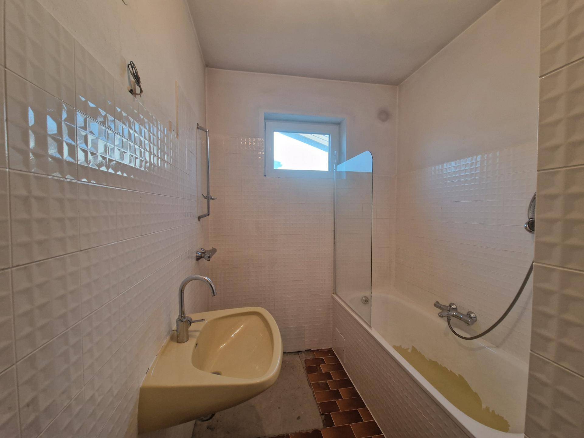Badezimmer mit Badewanne, Waschbecken und Fliesen in hellem Design, mit Fenster.