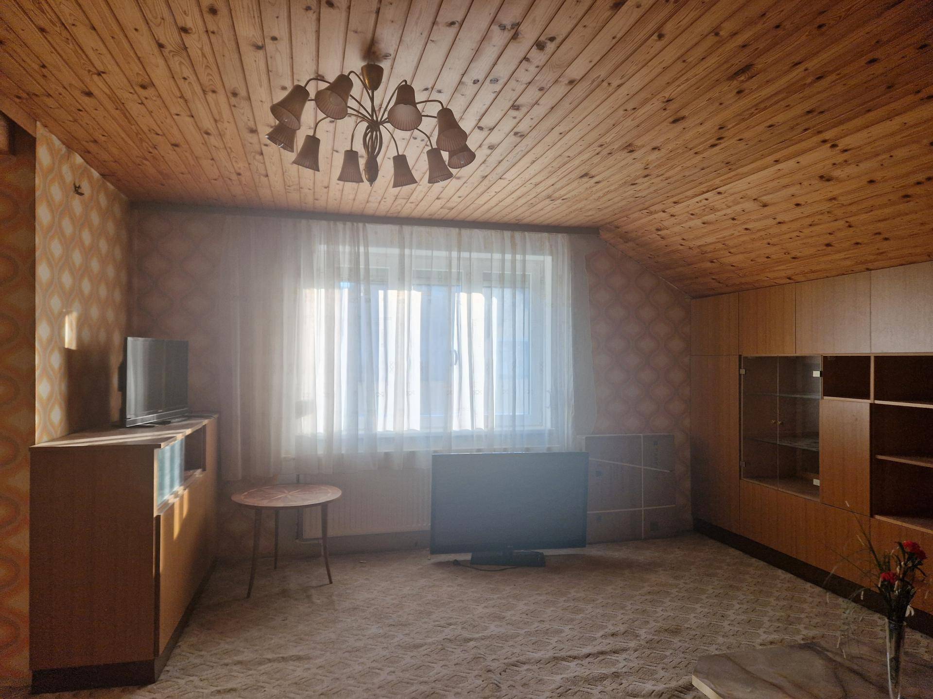 Gemütliches Wohnzimmer im Dachgeschoss mit Holzdecke, Teppichboden und Vintage-Möbeln.