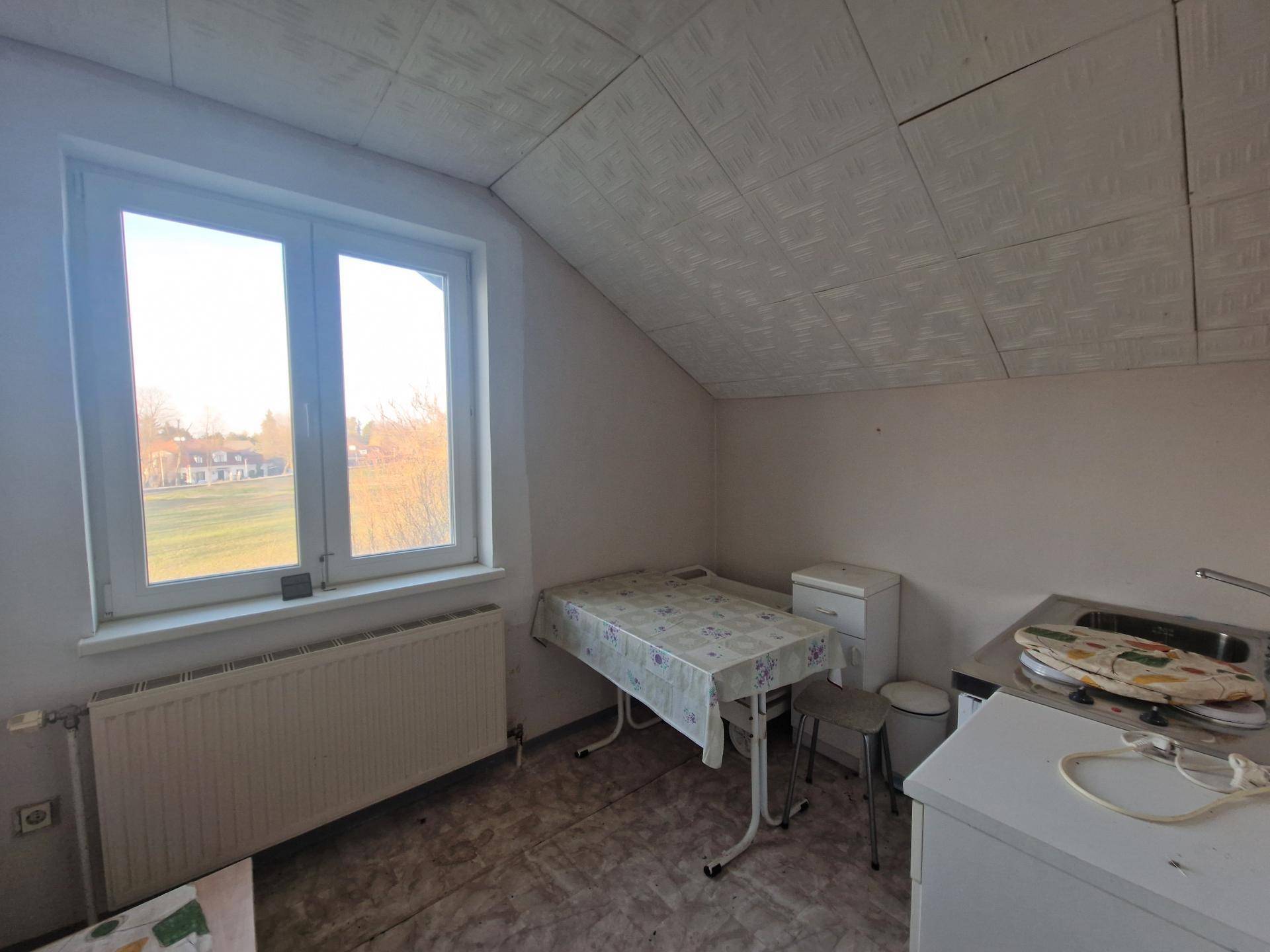 Einfache Küche im Dachgeschoss mit Fenster und kleiner Essecke, funktional eingerichtet.