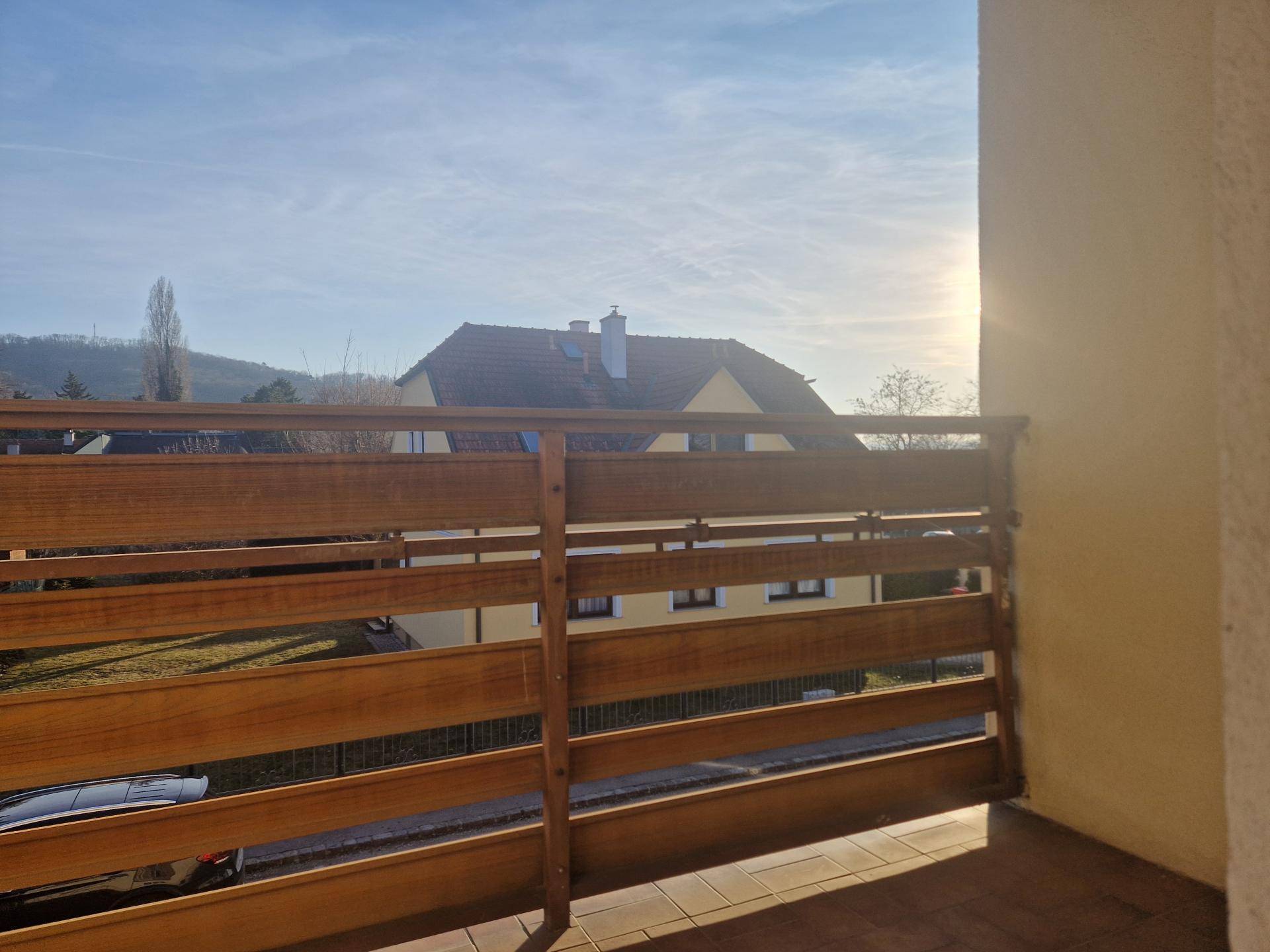 Sonniger Balkon mit Holzgeländer und Blick auf die umliegende Landschaft.