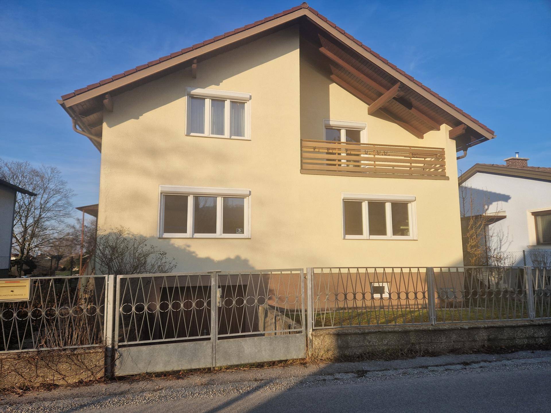Vorderansicht des Hauses mit Balkon, Rollläden und Metallzaun, gut gepflegt.