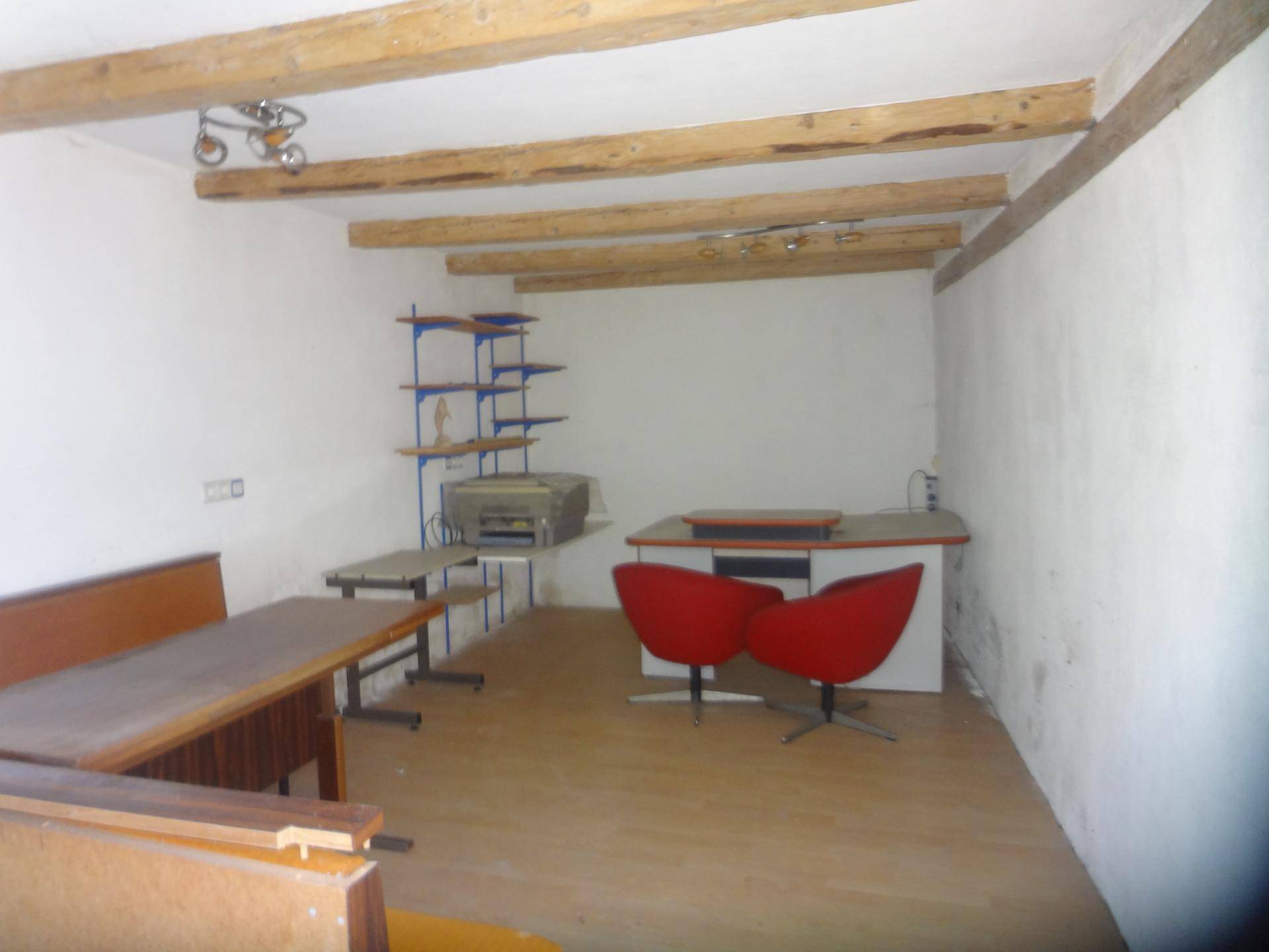 Einfacher Arbeitsraum mit Holzbalken, Schreibtisch und roten Stühlen.