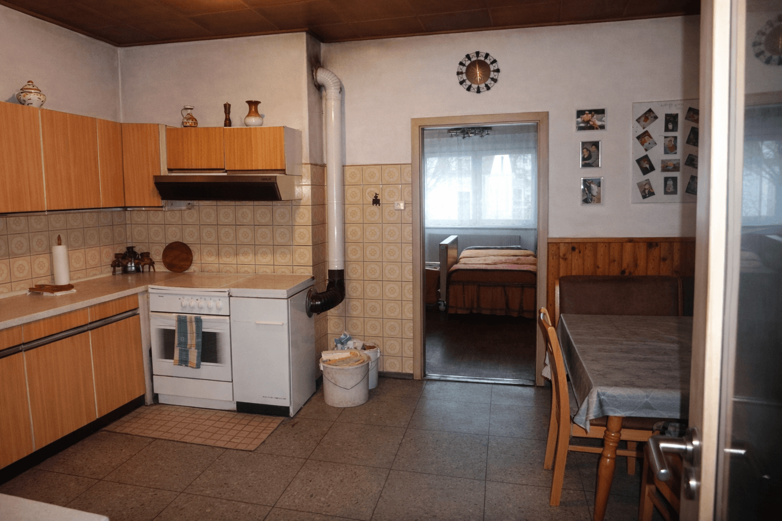 Rustikale Wohnküche mit Fliesenboden, Holzmöbeln und Blick in ein weiteres Zimmer.