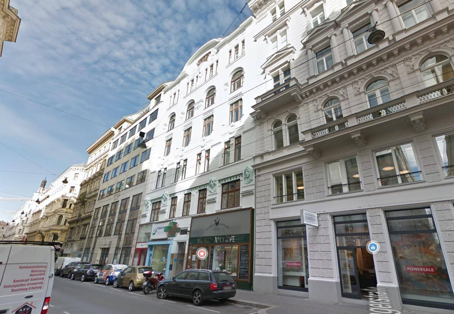 Historische Straßenansicht mit eleganten Gebäudefassaden und Geschäften im Erdgeschoss an einem sonnigen Tag.