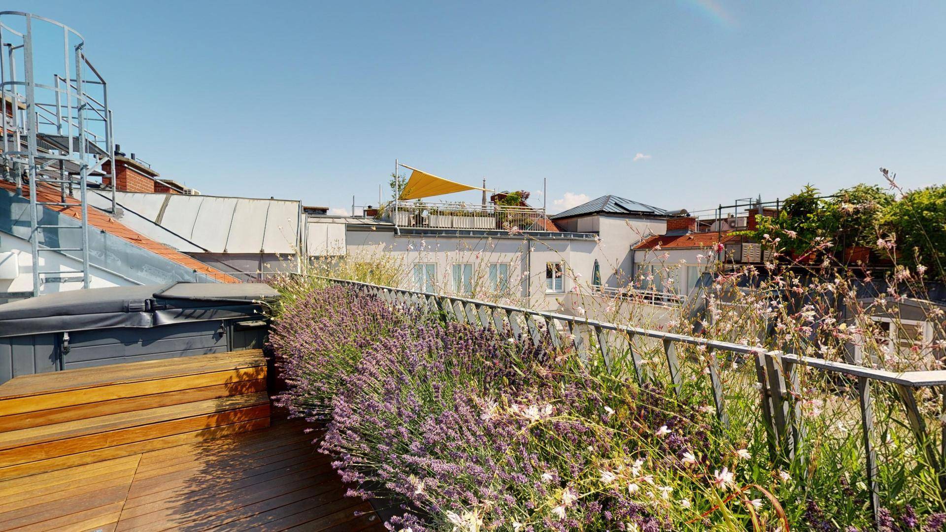 Dachterrasse mit Whirlpool, Holzdeck und Blick über die Dächer der Stadt an einem sonnigen Tag.