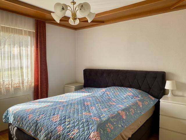 Schlafzimmer mit Holzbalkendecke, Doppelbett und Fenster mit Vorhängen.