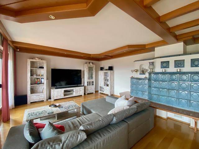 Gemütliches Wohnzimmer mit Holzbalkendecke, Kachelofen und modernem Sofa.