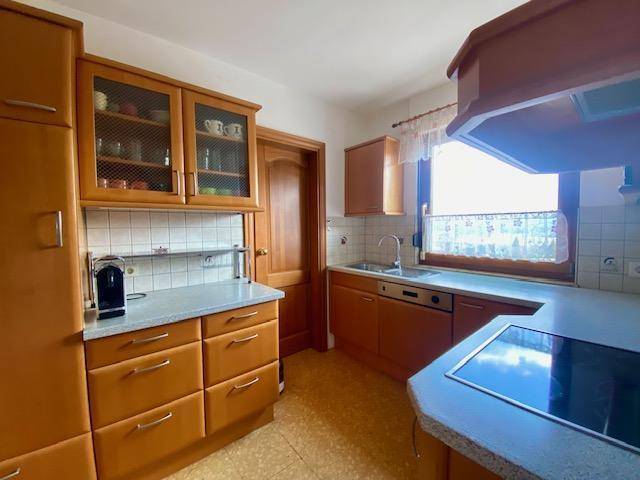 Funktionale Küche mit Holzschränken, Fliesenboden und Fenster mit Blick ins Grüne.
