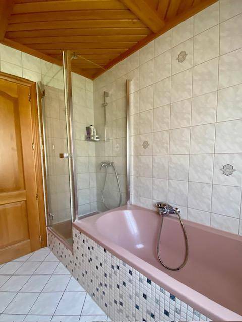 Badezimmer mit rosa Badewanne, Duschbereich und Fliesen im 80er-Jahre-Stil.