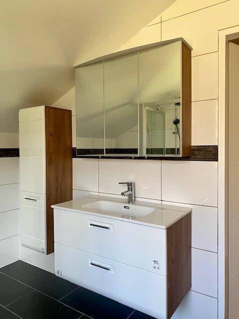 Modernisiertes Badezimmer mit weißem Waschtisch, Spiegelschrank und dunklen Bodenfliesen.
