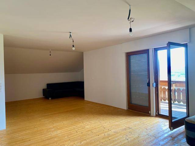 Geräumiger Wohnbereich im Dachgeschoss mit Holzboden und Zugang zu einem Balkon.