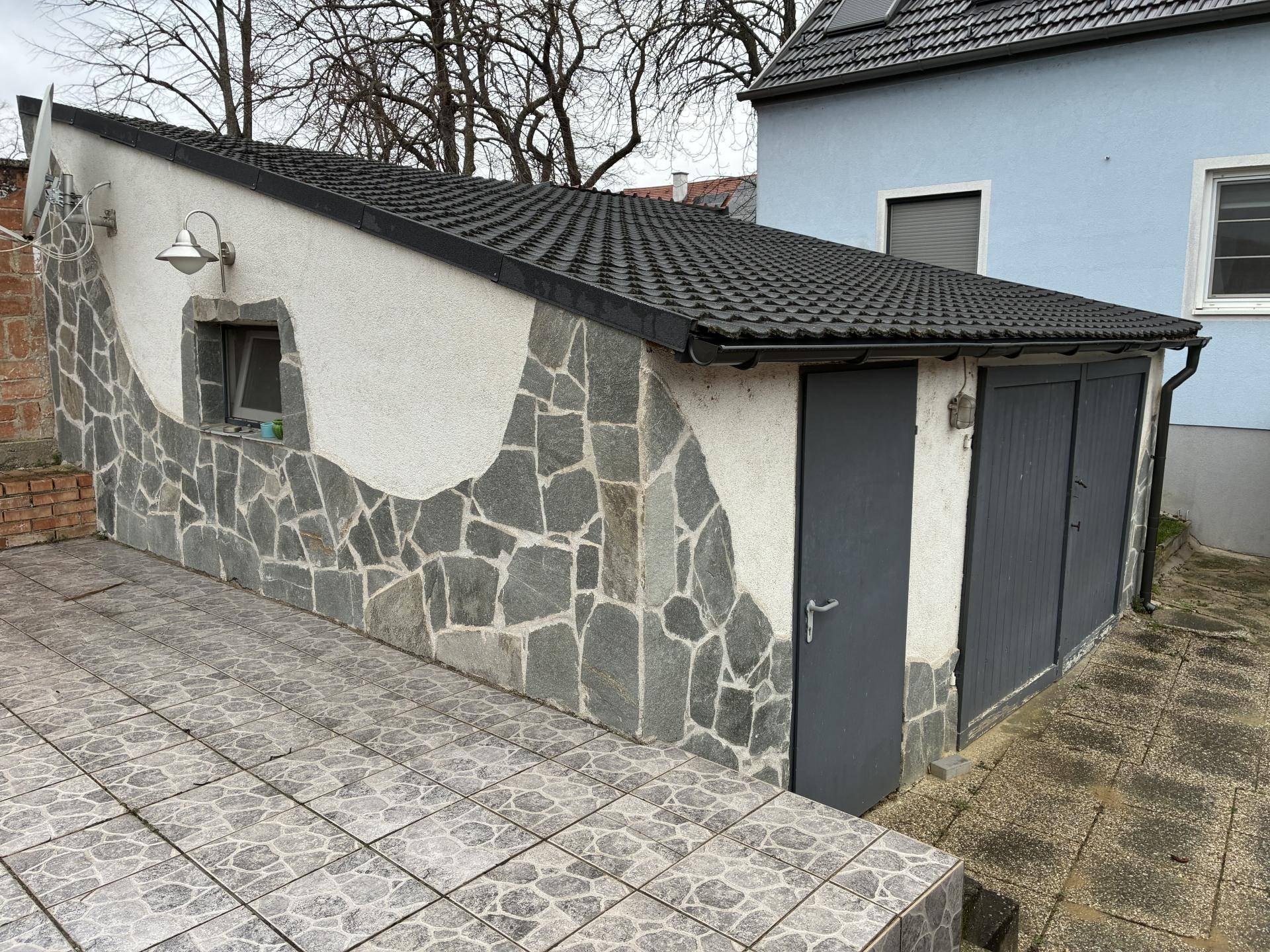 Robuste Garage mit Steinverkleidung und dunklem Ziegeldach, davor ein gepflasterter Bereich.