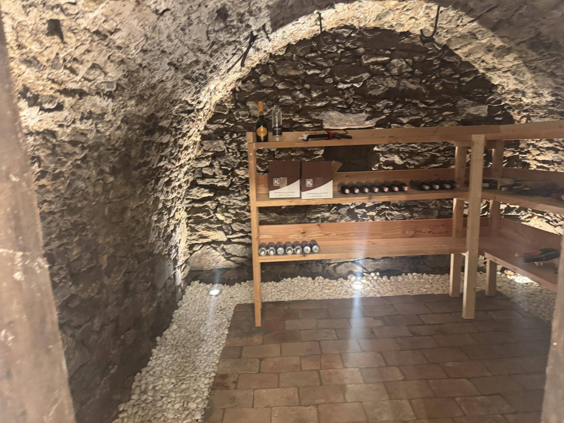 Rustikaler Weinkeller mit Steinwänden, Holzböden und Regalen zur Weinlagerung.