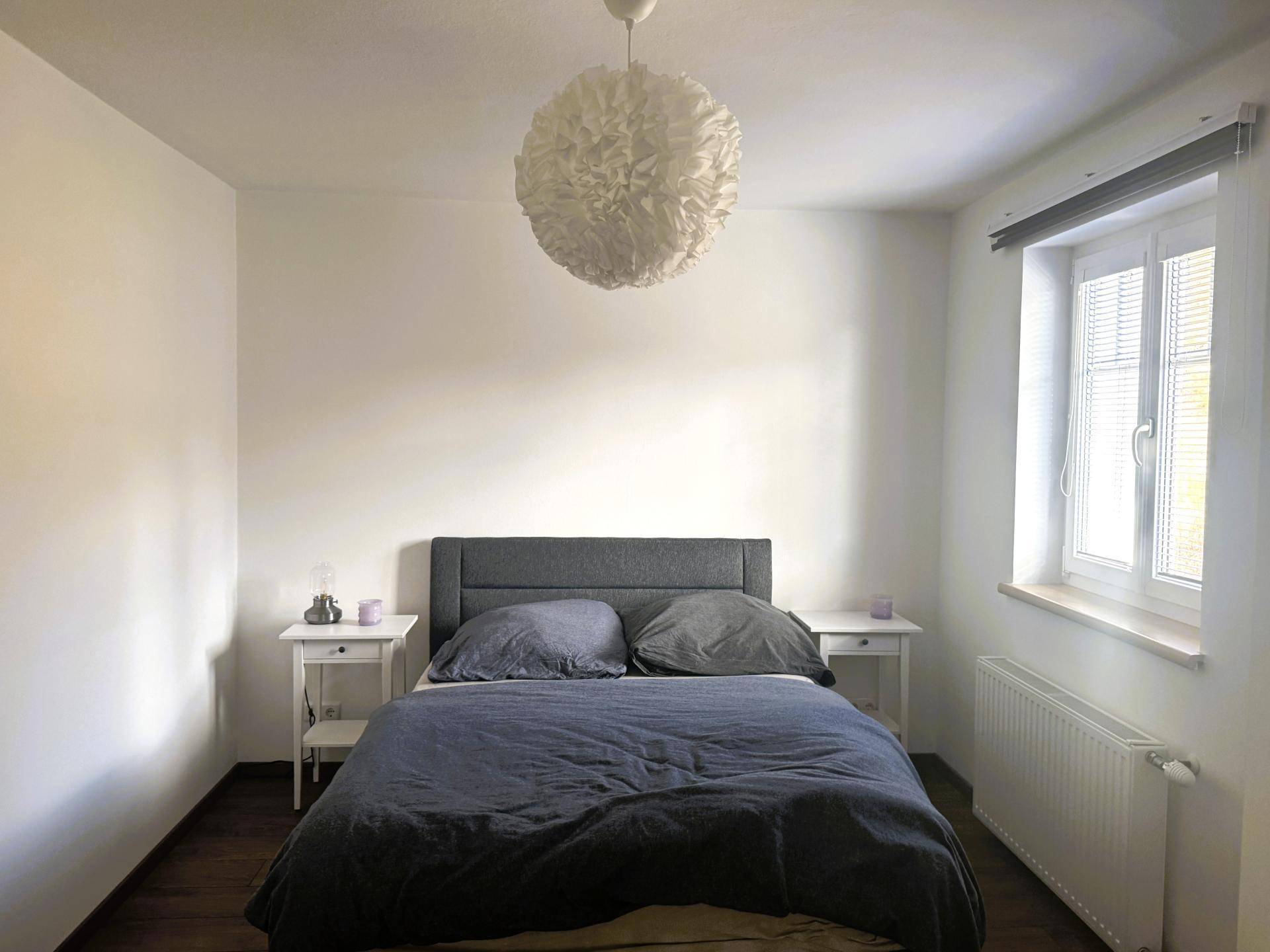 Ruhiges Schlafzimmer mit Doppelbett, Nachttischen und einem Fenster mit Jalousien.