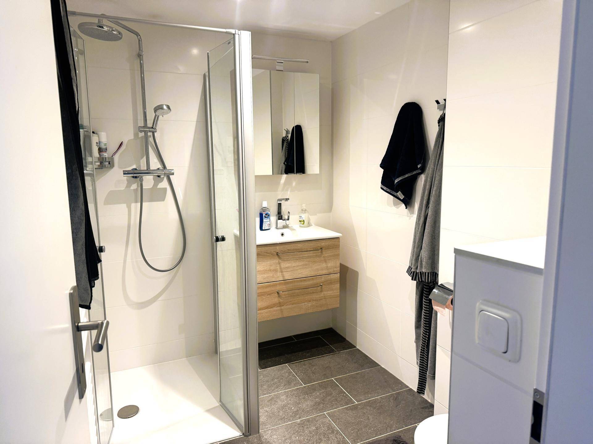 Modernes Badezimmer mit ebenerdiger Dusche, Waschtisch und hellen Fliesen.