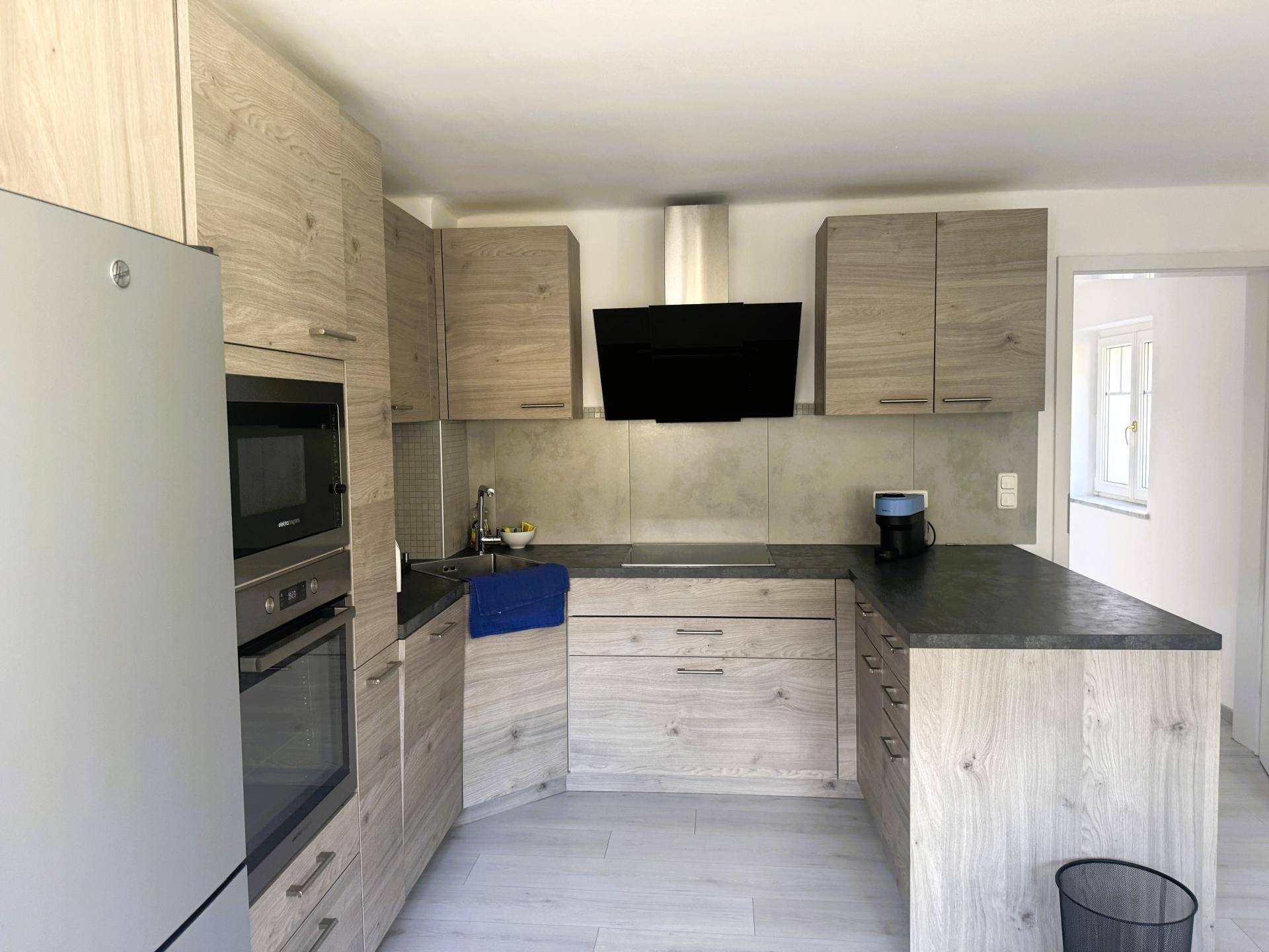 Moderne Einbauküche mit Holzoptik-Fronten, dunkler Arbeitsplatte und integrierten Geräten.